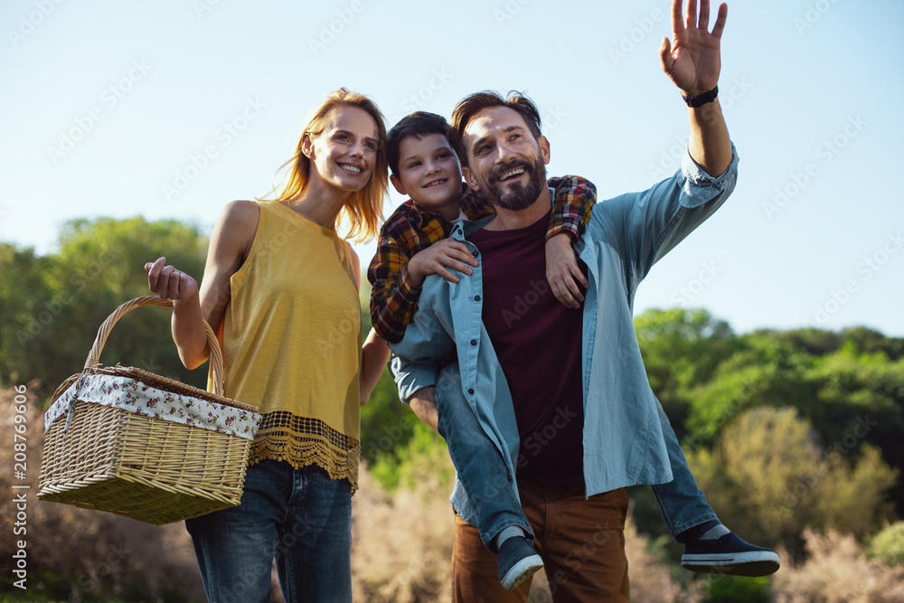 Great day. Delighted bearded father smiling and holding his son on his back Great day. Delighted bearded father smiling and holding his son on his back
