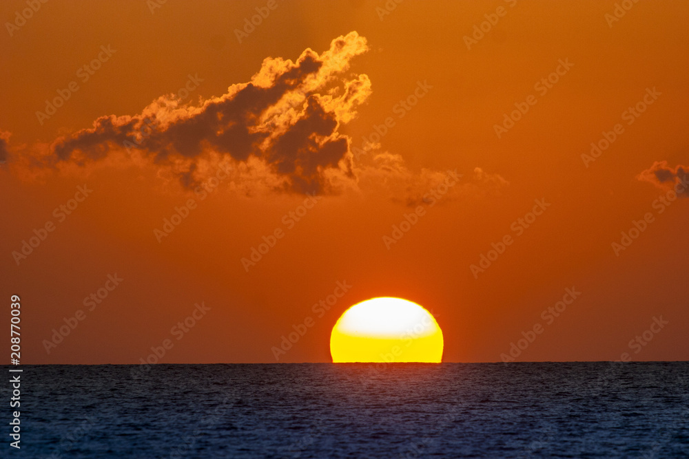 sun diving into the sea as big red boule, sailing yacht sailing straight into the sun