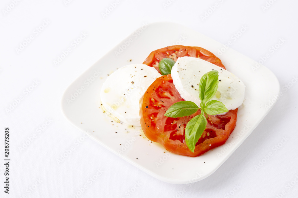 Mozzarella and tomatoes with basil on a white square plate. The background is white. Copiespice. Mozzarella and tomatoes with basil on a white square plate. The background is white. Copiespice.