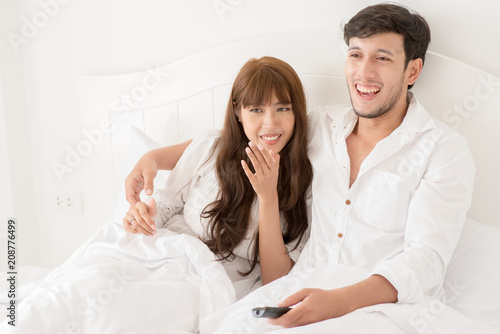 An attractive young couple lying in bed and watching movie.