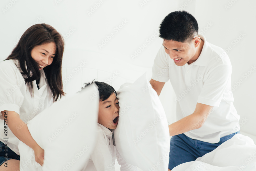Happy family playing in battle of pillows on bed.