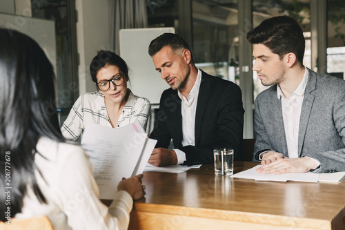 Business, career and recruitment concept - team of employers in formal wear sitting at table in office, and interviewing woman for job in big corporation photo