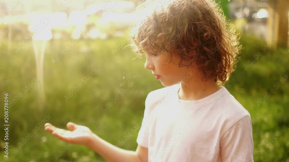 Closed portrait of a curly-haired boy. The schoolboy stands under the summer rain and puts his hand to the drops. Warm rain. Childrens Day
