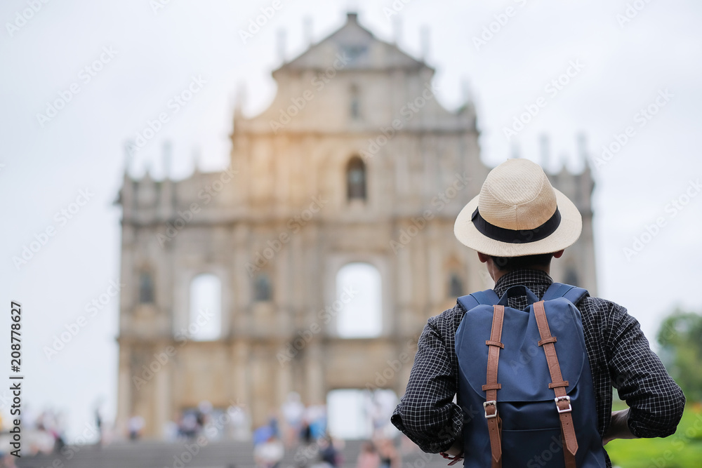 Young man traveling backpacker with hat, Asian hipster traveler looking to Ruins of St. Paul's, Historic Centre of Macau, a UNESCO World Heritage Site. landmark and popular for tourist attractions 