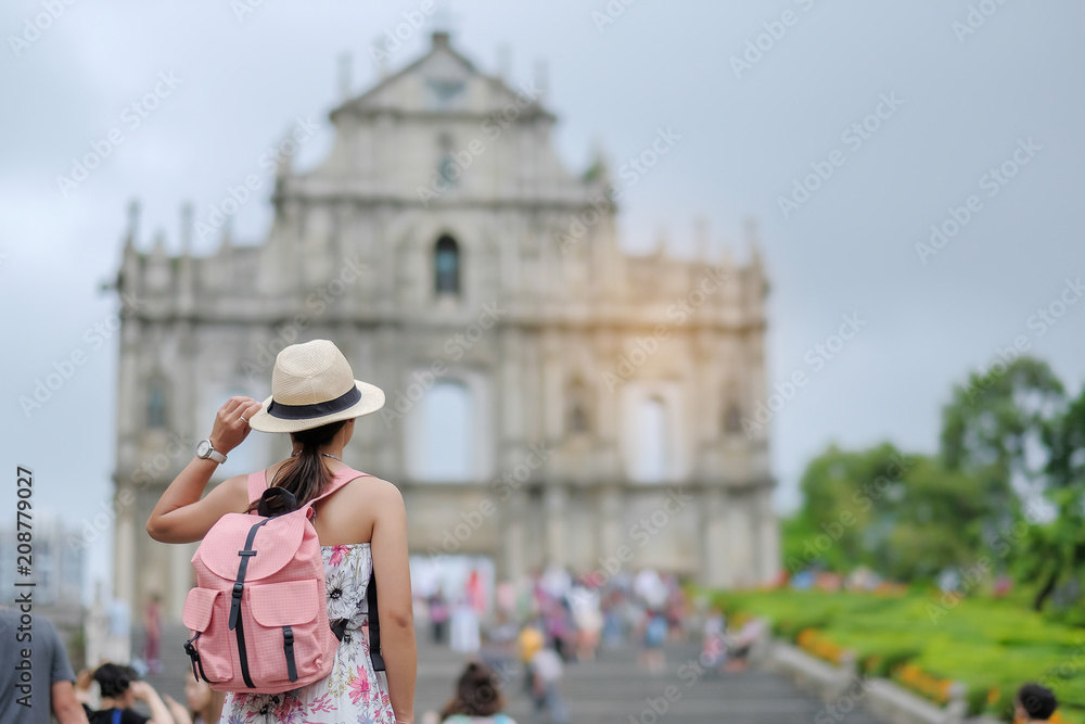 Young woman traveling backpacker with hat, Asian hipster traveler looking to Ruins of St. Paul's, Historic Centre of Macau, a UNESCO World Heritage Site. landmark and popular for tourist attractions 