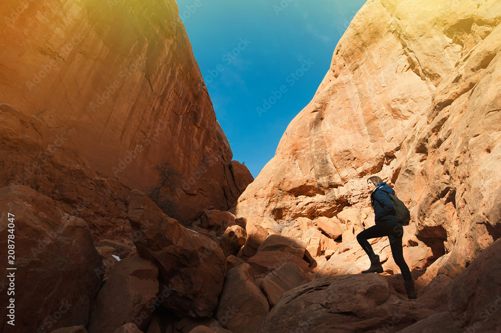 Beautiful woman with backpack hiking along a scenic canyon overlook in Arches National Park in Utah Beautiful woman with backpack hiking along a scenic canyon overlook in Arches National Park in Utah