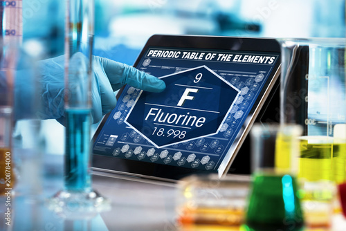 scientist consulting on the digital tablet data of the chemical element Fluorine F / researcher working on the computer with the periodic table of elements 