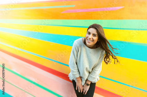 Young beautiful caucasian woman posing outdoor in the city, near a colorful wall, looking at camera