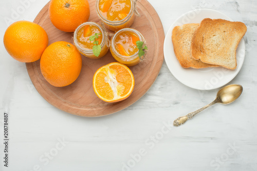 Orange jam in a glass jar on a light background with toasts. With empty space for writing