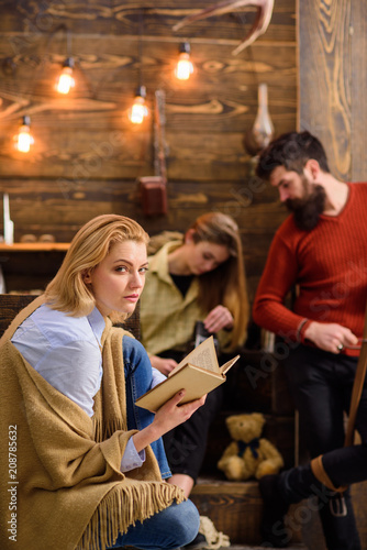 Woman with blond hair and cunning look reading favorite novel. Wife of lumberjack enjoying new book. Bearded man sharpening knife and chatting to daughter. Vacation in rural area, out of town concept