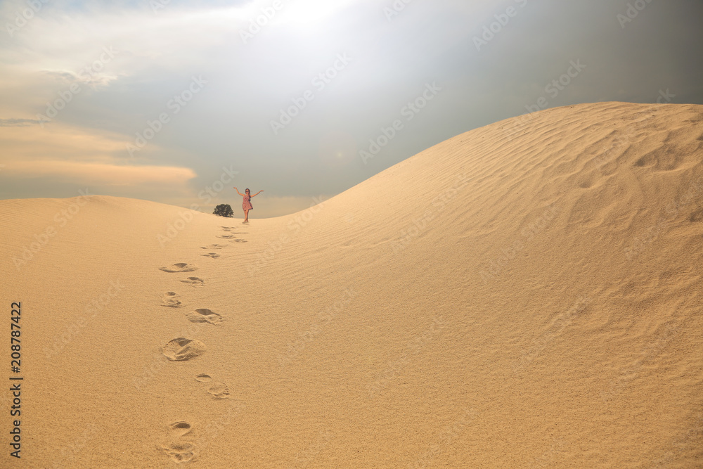 Młoda dziewczyna spaceruje po piaszczystej wydmie.