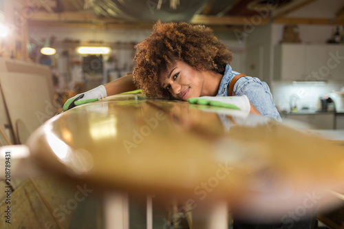 Happy young woman working on surfboard in her workshop