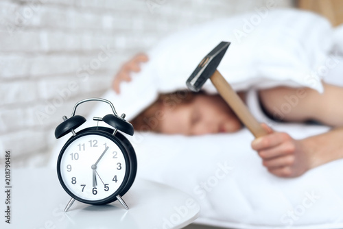 Young red haired man hammers alarm clock.