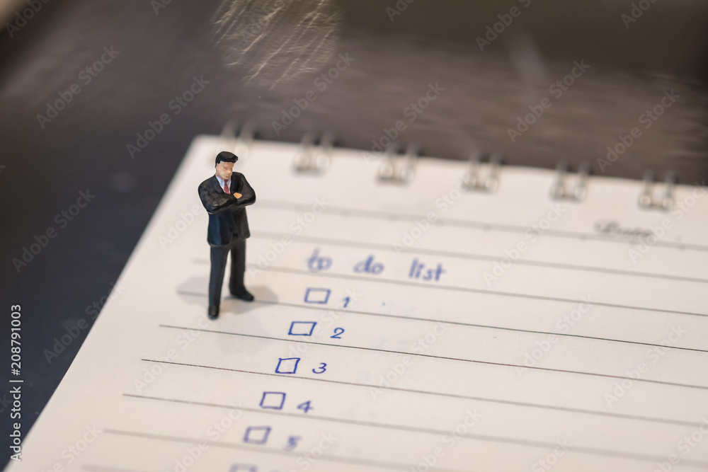 Business and planning concept. Businessman miniature figure standing on notebook with hand writing to do list. Business and planning concept. Businessman miniature figure standing on notebook with hand writing to do list.