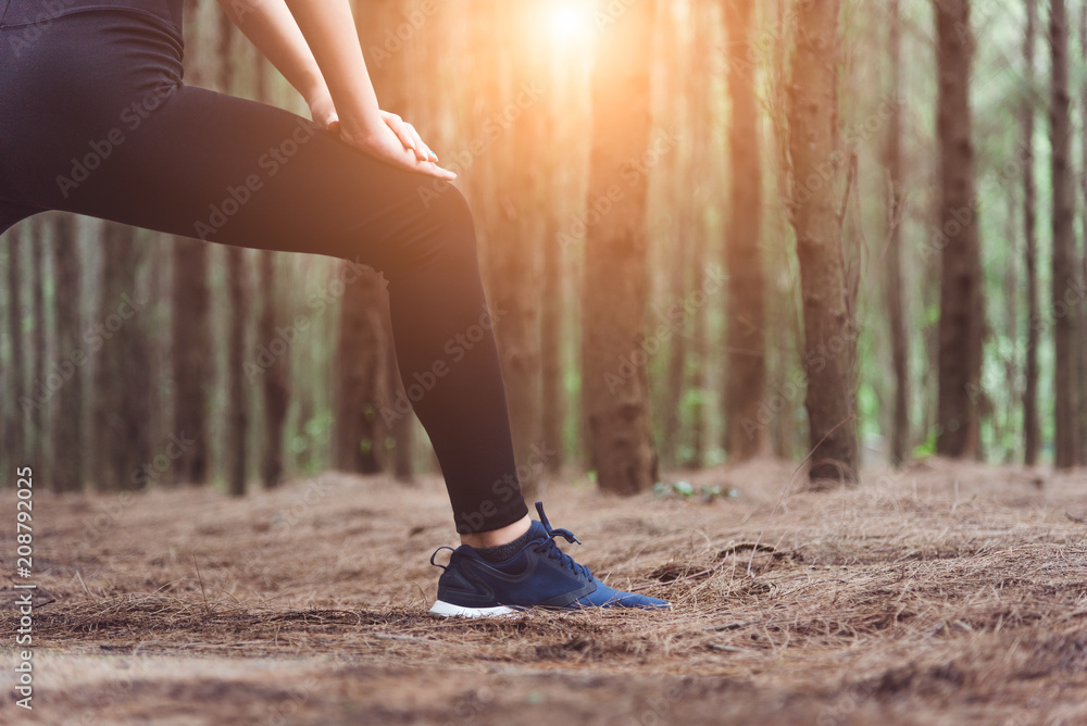 Close up of lower body of woman doing yoga and stretching legs before running in forest at outdoors. Sports and Nature concept. Lifestyle and Activity concept. Pine woods theme. Close up of lower body of woman doing yoga and stretching legs before running in forest at outdoors. Sports and Nature concept. Lifestyle and Activity concept. Pine woods theme.