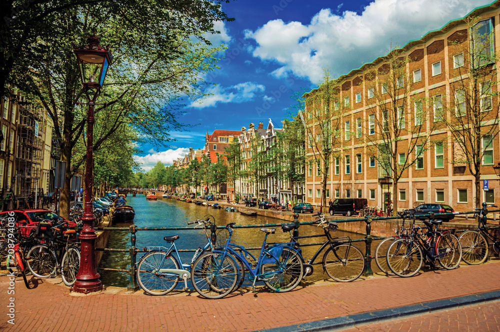 Bridge on canal with iron balustrade, old buildings and bicycles in Amsterdam. Famous for its huge cultural activity and full of graceful canals. Northern Netherlands. Retouched photo.