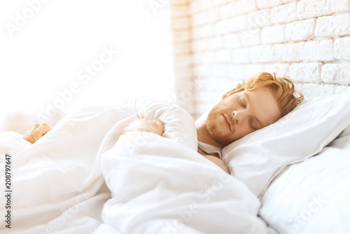 Young redhead man sleeps under white blanket.