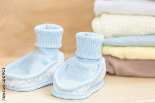 Little blue shoes - booties and clothes on natural wooden background. Pastel clothes for baby infant. Newborn. Home cosiness.