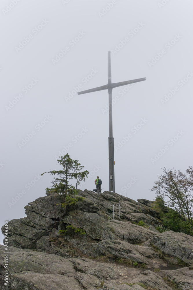 Woman in the fog stands next to the huge summit cross