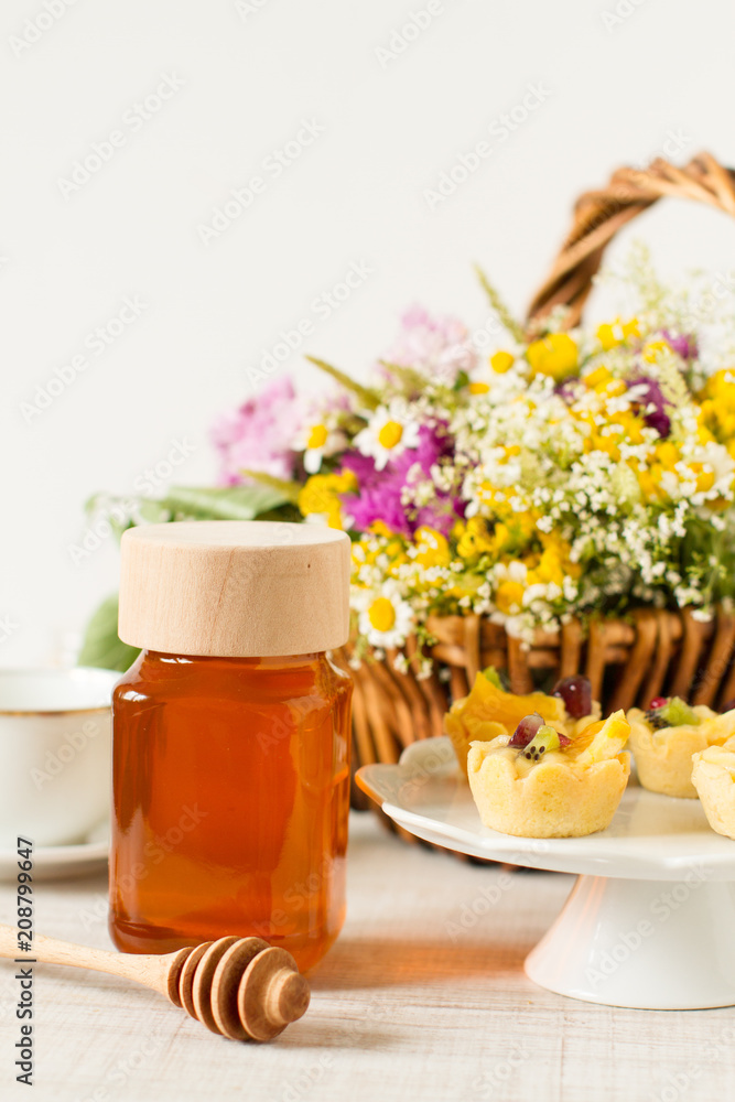 Jar of honey on a table with flowers, dessert and other ingredients