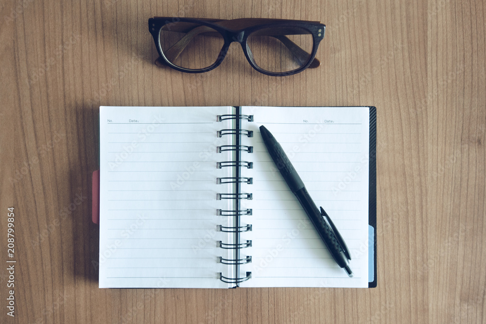 Top view on a note book with pen and glasses on a workdesk Top view on a note book with pen and glasses on a workdesk