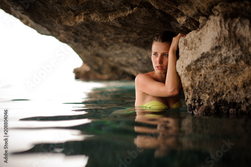 Young and beautiful wet woman dressed in yellow swimsuit near the rock