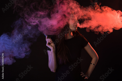 young woman smoking electronic cigarette on dark background