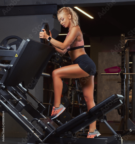 Beautifull fitness woman in sportswear posing near the legs press machine in a gym.
