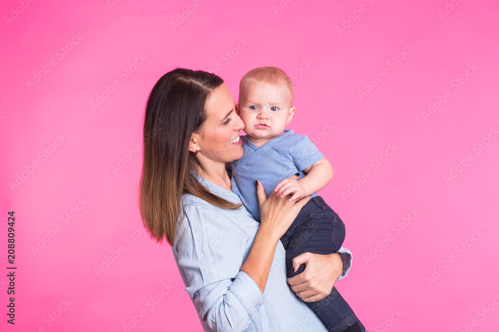 Loving mother playing with her baby boy on pink background