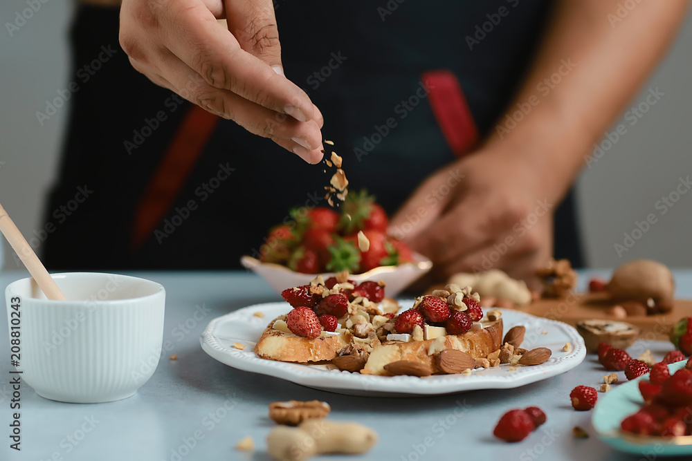 Sweet sandwiches with little strawberries, cheese, camembert, brie, nuts and honey on the whole grain bread bruschetta cooking by chef hand on light background
