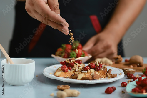 Sweet sandwiches with little strawberries, cheese, camembert, brie, nuts and honey on the whole grain bread bruschetta cooking by chef hand on light background
