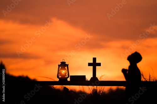 The boy sit and praying to God with oil lamp and cross, christian concept.