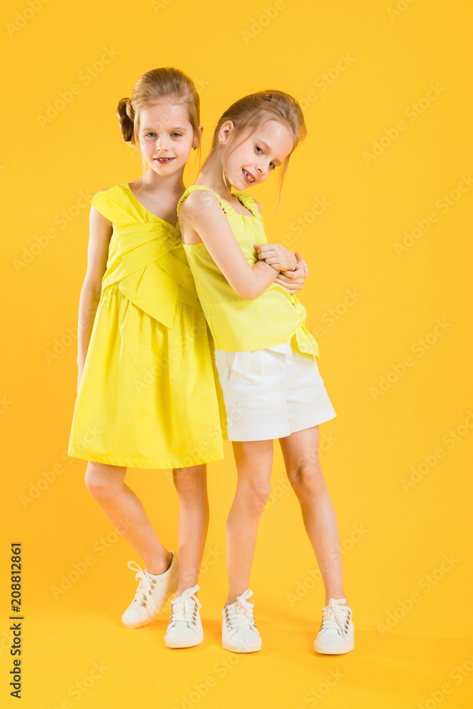 The girls of the twins stand together on a yellow background. The girls of the twins stand together on a yellow background.