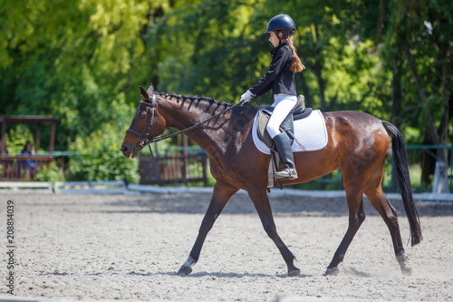 Teenage girl riding bay horse performing dressage test on equestrian competition © skumer