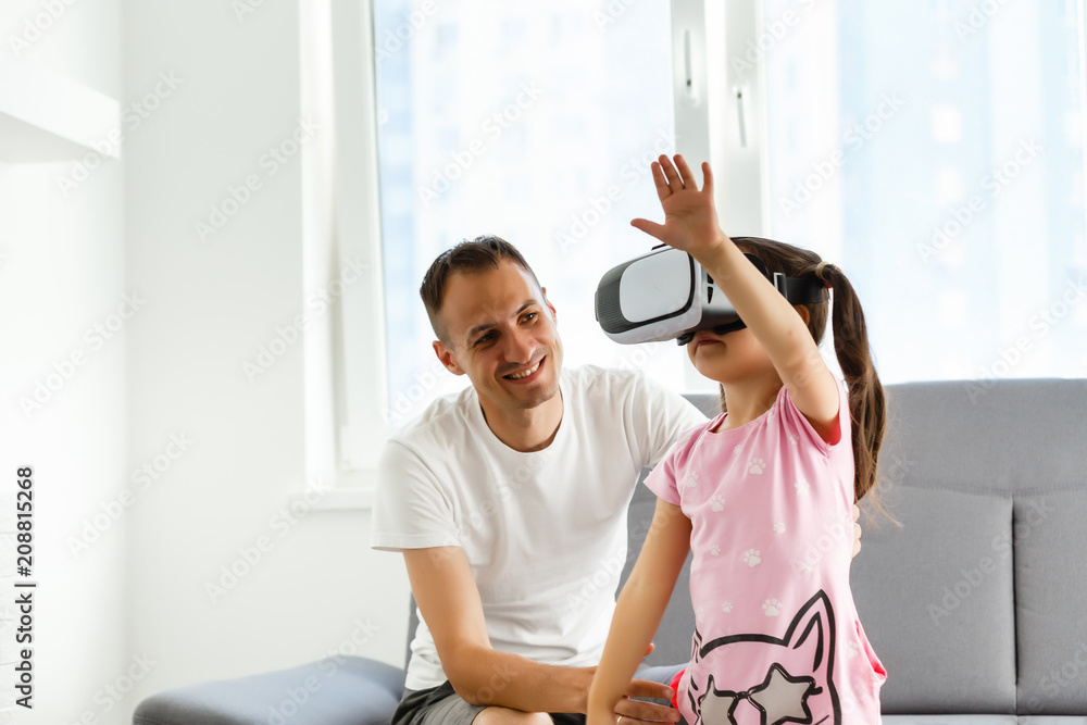 Father and daughter spend time together. The girl is looking into virtual reality glasses. A man and a little girl are playing with virtual reality. Father and daughter spend time together. The girl is looking into virtual reality glasses. A man and a little girl are playing with virtual reality.