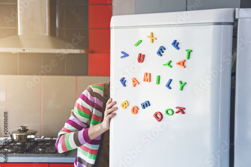 Woman looking in open fridge with Family letters on door. Cooking for children and husband concept photo