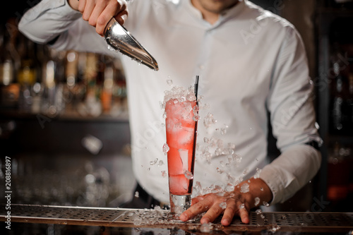 Barman adding ice cubes into the glass with strawberry mojito summer cocktail