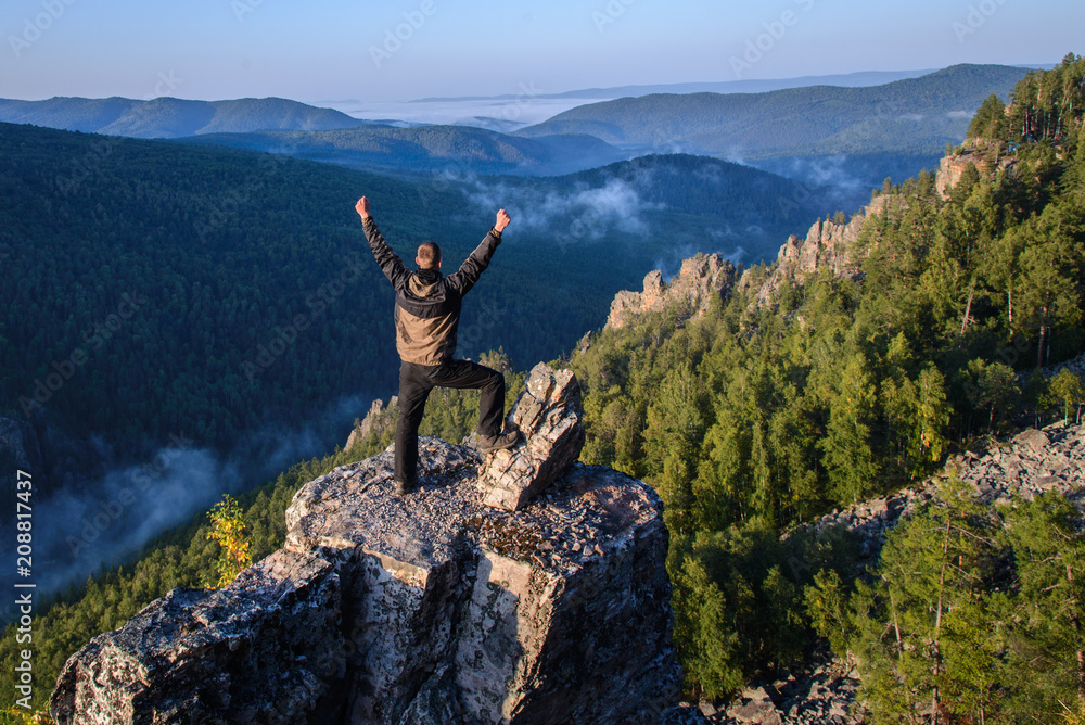 Happy man traveller standing with raised hands on mountain top and celebrating success.