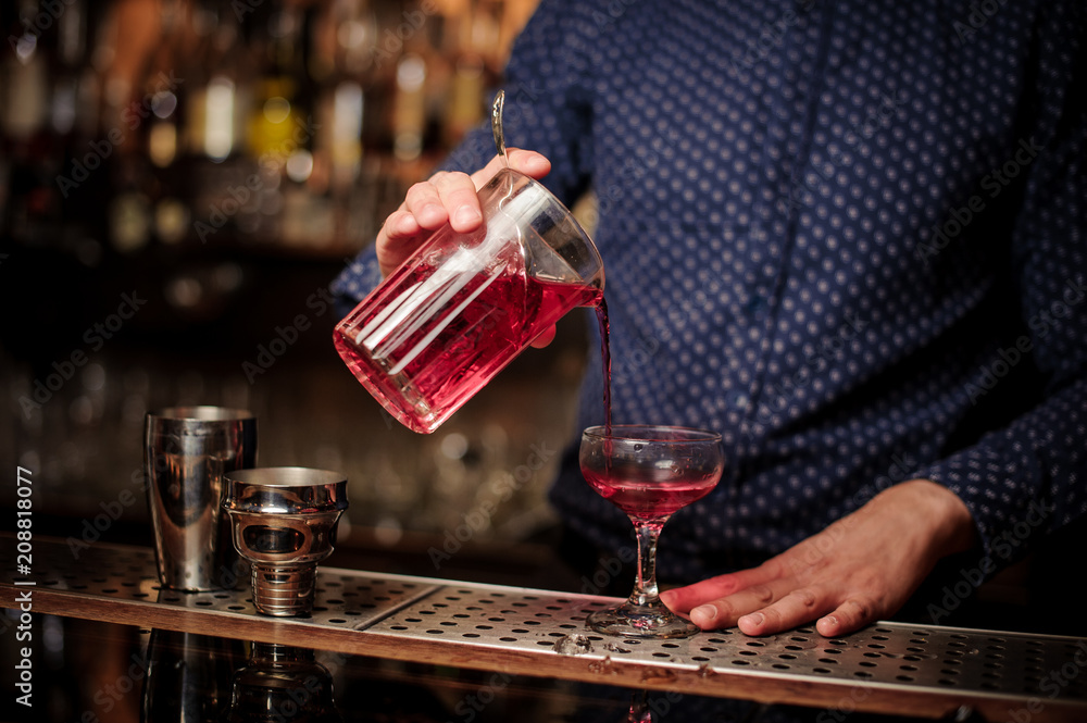 Bartender pouring fresh and sweet pink summer cocktail into the glass