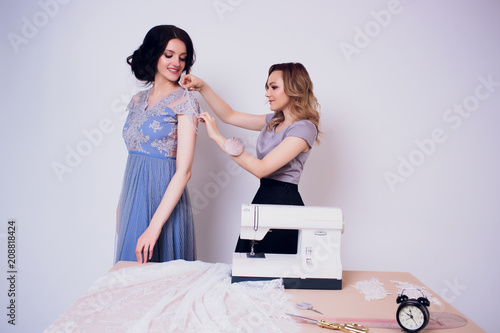 beautiful woman seamstress with long hair and customer. tailor creates image for customer in sewing workshop. dressmaker measures girl with measuring tape . Concept Fashion Design photo