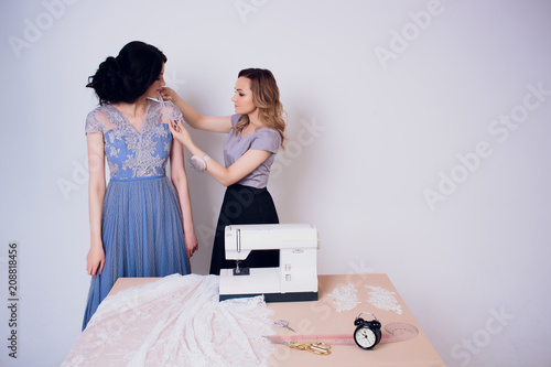 beautiful woman seamstress with long hair and customer. tailor creates image for customer in sewing workshop. dressmaker measures girl with measuring tape . Concept Fashion Design photo