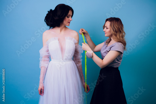 beautiful woman seamstress with long hair and customer. tailor creates image for customer in sewing workshop. dressmaker measures girl with measuring tape . Concept Fashion Design photo