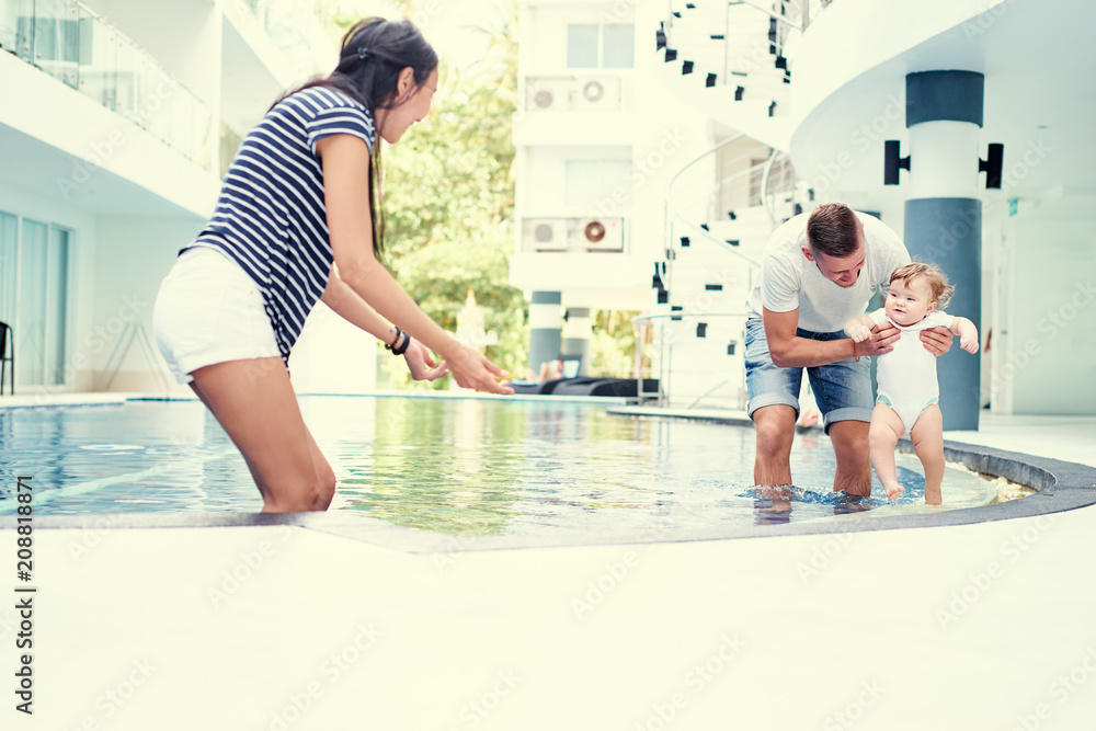 Naklejka premium Family holiday. Father, mother and little daughter playing together at swimming pool.