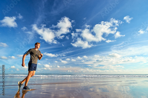 Sports lifestyle. Happy young man in earphones jogging on the sea shore.