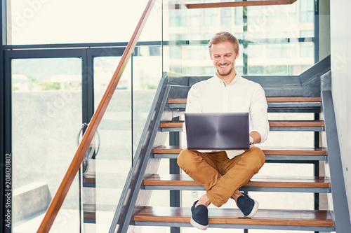 Freelance and technology. Handsome young man working on laptop computer siitting on stairs indoor. photo