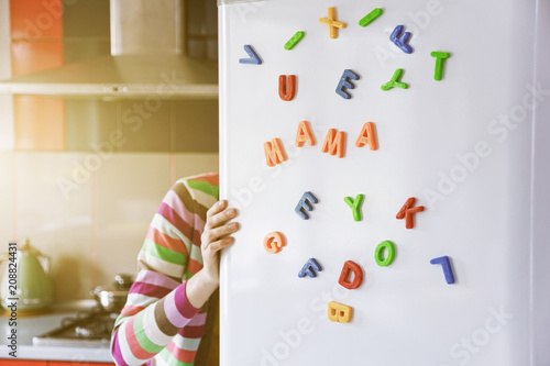 Woman looking in open fridge with Mama letters on door. Cooking for family and children concept