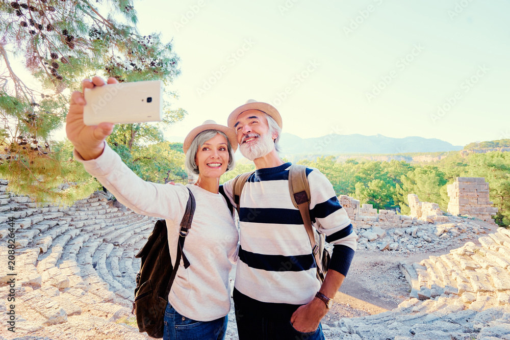 Tourism and technology. Traveling senior couple taking selfie together against ancient sightseeing background. - obrazy, fototapety, plakaty 