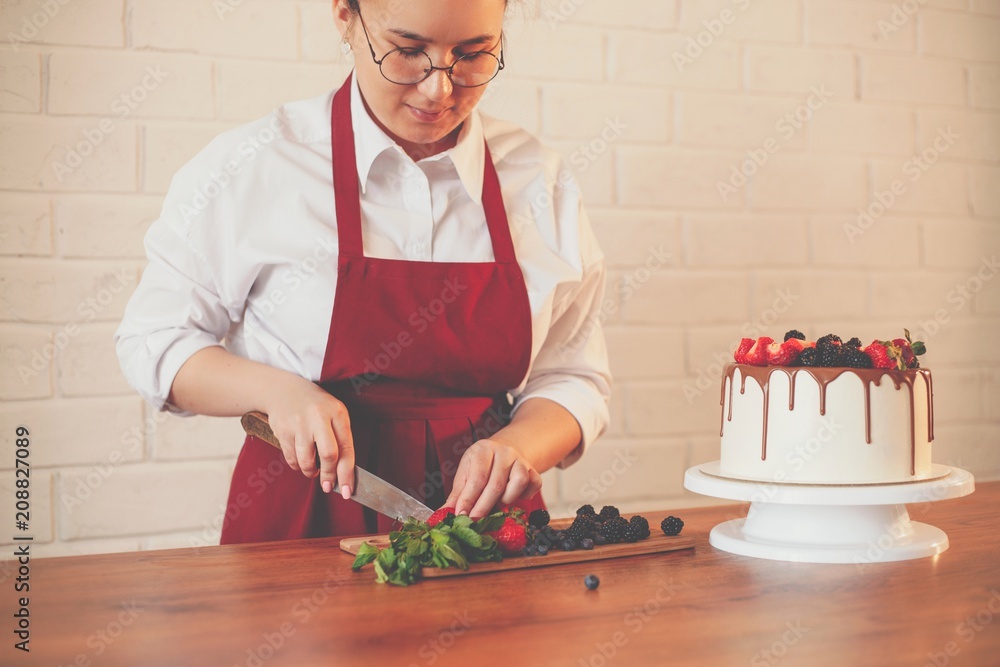 Girl confectioner cuts fresh berries with a knife to decorate the cake