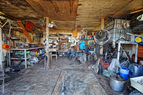 Inside a messy and cluttered garage shed with tools, cans, garden equipment in organised chaos