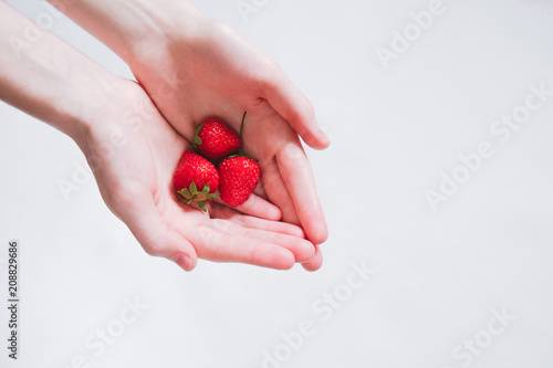 Female hands holding handful of strawberries on white background, close up